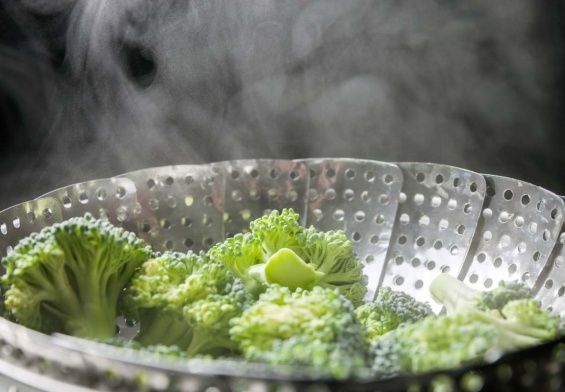 Freshly steamed green broccoli in skimmer pot with steam